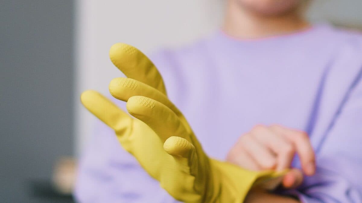 Personne enfilant des gants de protection jaunes avant un nettoyage de logement, dans une pièce lumineuse.